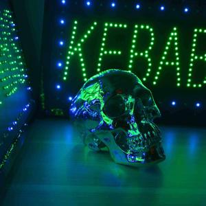 A mirror-like metalic skull sits between two neon signs that read "KEBABS"